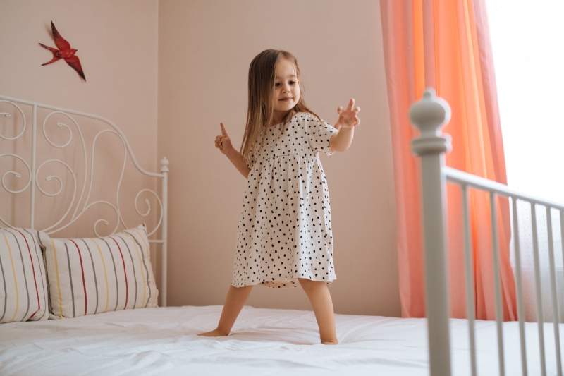 Happy little child girl in motion jumping on bed alone flying in air feeling joy.